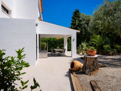 Terraza cubierta con comedor exterior, rodeada de jardín mediterráneo y gravilla blanca.