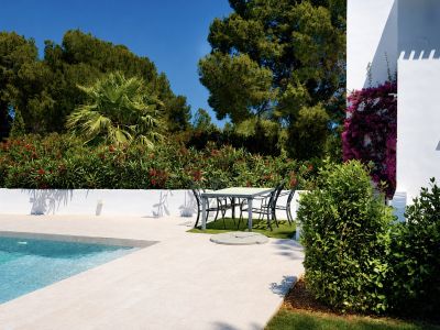 Vista de la piscina con borde de piedra clara y área de comedor exterior rodeada de vegetación.