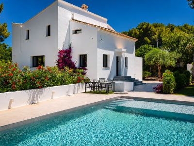 Vista de la piscina turquesa con acceso escalonado y la fachada blanca de la villa con buganvillas.