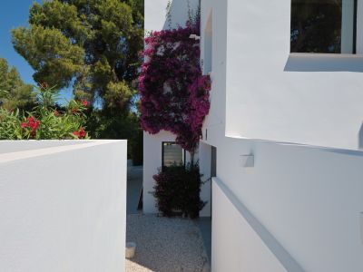 Vista exterior de la villa, con buganvillas floreciendo en la fachada blanca y grava clara en el suelo.