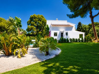 Vista exterior de la villa con fachada blanca, jardín con césped y vegetación tropical.
