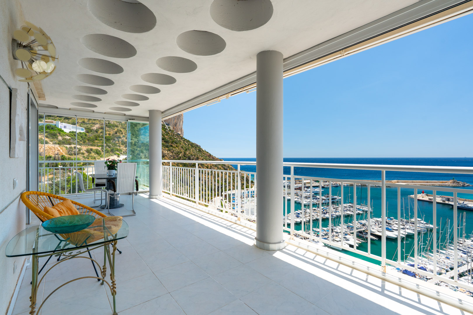 Amplia terraza cubierta con suelo de baldosas claras, techo con detalles circulares y vistas panorámicas al puerto deportivo de Calpe, el mar Mediterráneo y el Peñón de Ifach.
