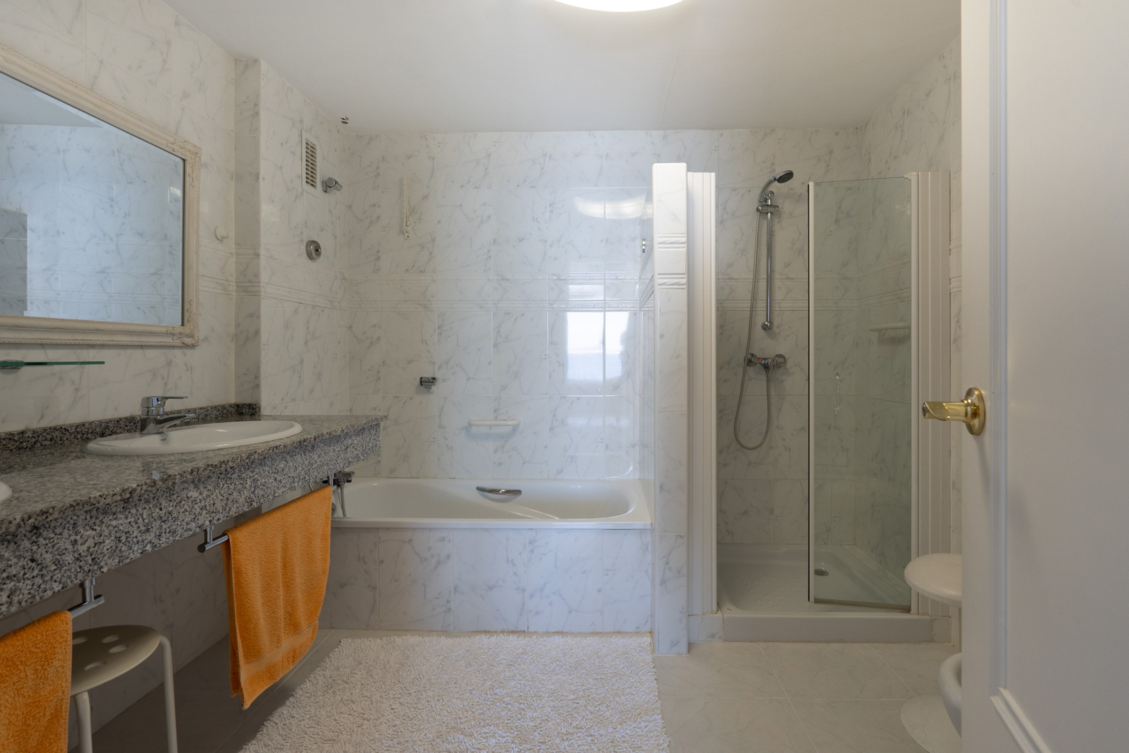Baño principal con azulejos efecto mármol, encimera de granito con lavabo, bañera y cabina de ducha independiente de cristal.