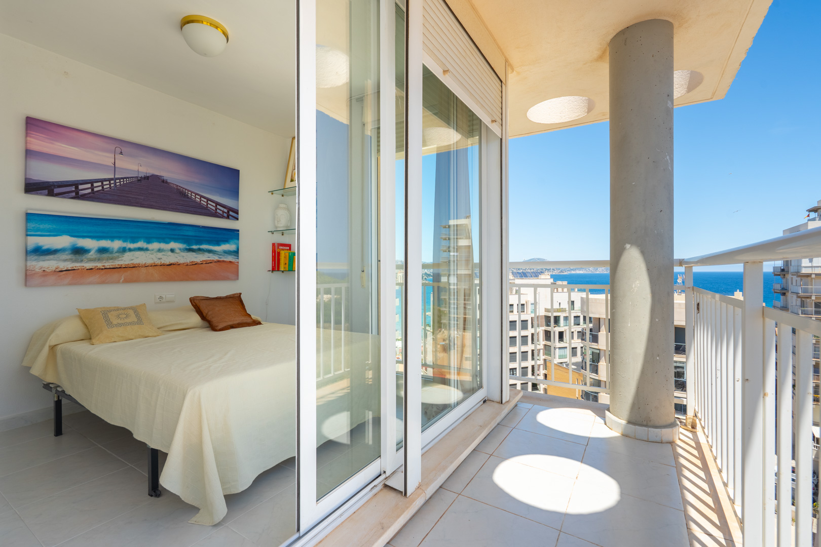Luminoso dormitorio con acceso directo a un balcón privado, destacando las puertas correderas de cristal, barandillas blancas y vistas al mar.