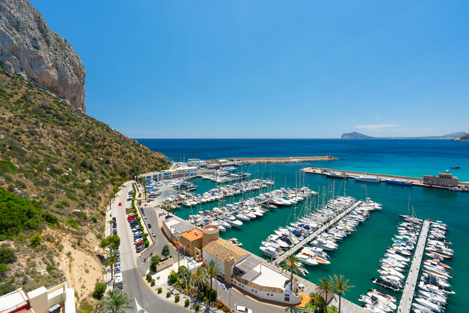 Vista panorámica del animado puerto deportivo de Calpe, con numerosos yates en el mar turquesa y el majestuoso Peñón de Ifach a la izquierda.