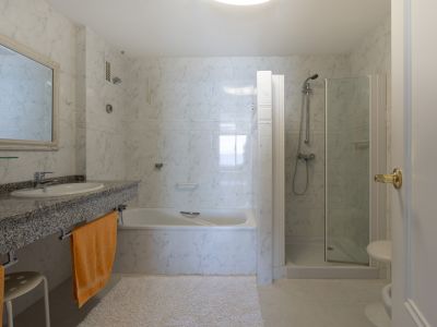 Baño principal con azulejos efecto mármol, encimera de granito con lavabo, bañera y cabina de ducha independiente de cristal.