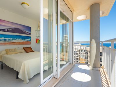 Luminoso dormitorio con acceso directo a un balcón privado, destacando las puertas correderas de cristal, barandillas blancas y vistas al mar.