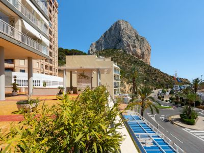 Vista del icónico Peñón de Ifach y la carretera costera, enmarcada por palmeras y vegetación en primer plano, desde la terraza del complejo.