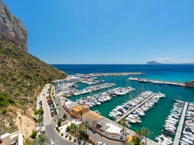 Vista panorámica del animado puerto deportivo de Calpe, con numerosos yates en el mar turquesa y el majestuoso Peñón de Ifach a la izquierda.