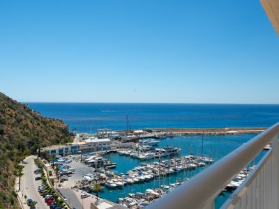 Vista panorámica desde el balcón, mostrando el animado puerto deportivo de Calpe con yates, el vasto mar Mediterráneo y la ladera verde.