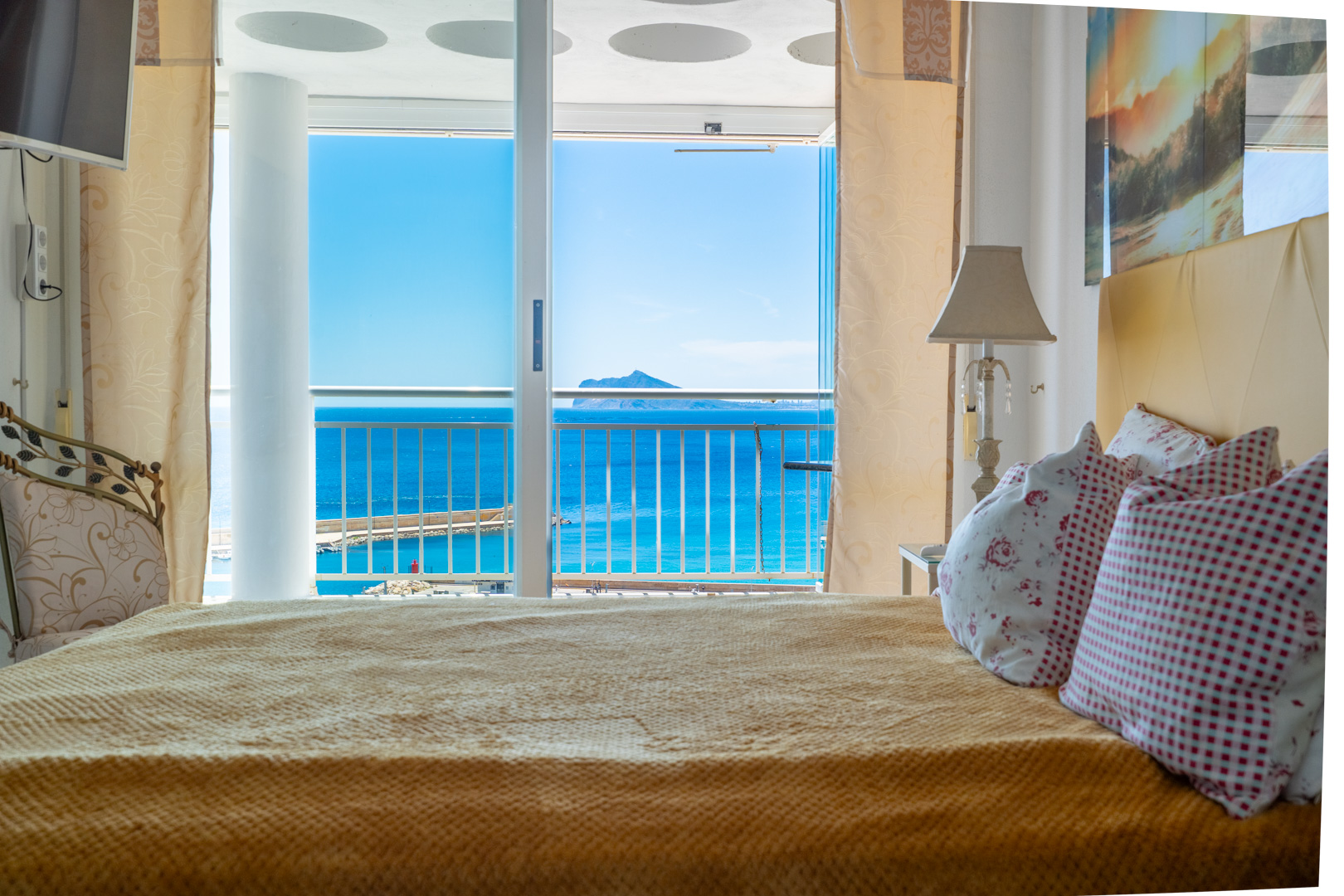 Dormitorio con cama acogedora y acceso directo a una terraza privada, ofreciendo vistas panorámicas al mar, el puerto y una isla lejana.