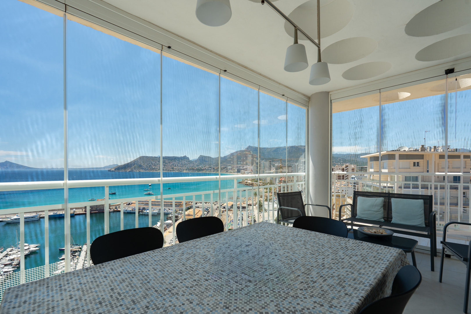 Terraza acristalada con zona de comedor, ofreciendo vistas directas al puerto deportivo de Calpe, el mar turquesa y el icónico Peñón de Ifach.