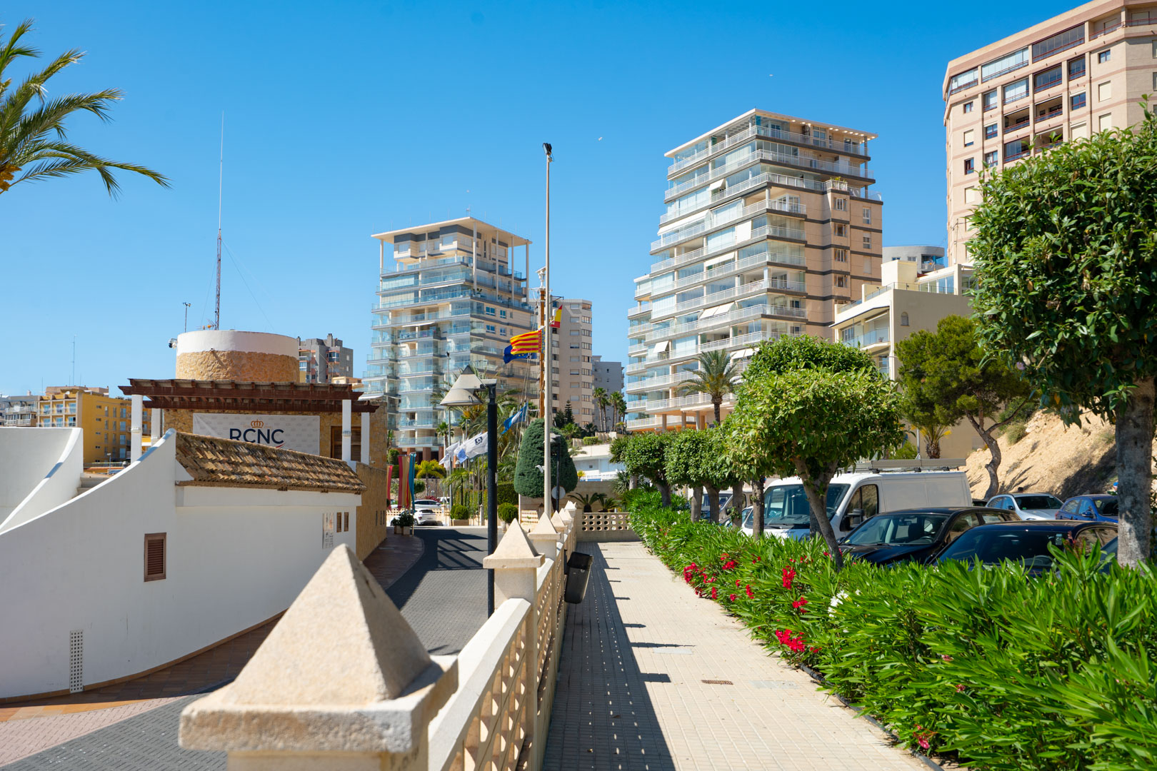 Vista del animado paseo marítimo de Calpe, con modernos edificios de apartamentos y el Real Club Náutico bajo un cielo azul despejado.