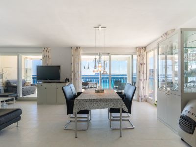 Amplio salón-comedor de planta abierta con suelos de baldosas claras, mesa de comedor moderna y vistas directas al mar a través de grandes puertas de cristal que dan a una terraza acristalada.