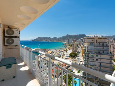 Balcón con vistas panorámicas al puerto deportivo de Calpe, la bahía turquesa y la costa urbana, enmarcado por una barandilla blanca y unidades exteriores de aire acondicionado.