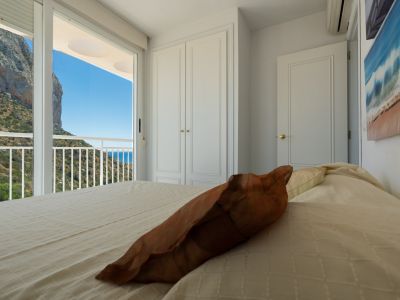 Dormitorio con acceso a balcón, ofreciendo vistas directas al icónico Peñón de Ifach, la exuberante ladera y el mar Mediterráneo. Incluye un armario empotrado blanco.