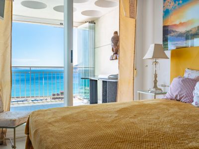 Dormitorio con cama de tonos mostaza y acceso directo a una terraza acristalada, ofreciendo vistas panorámicas al mar y al puerto.