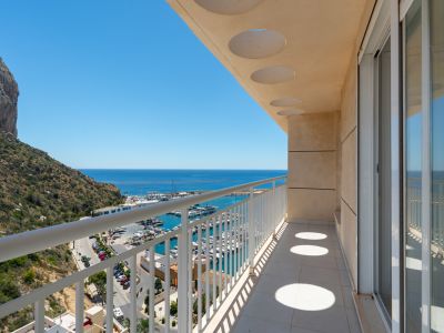 Espaciosa terraza privada con suelo de baldosas y barandilla blanca, con techo de diseño circular. Ofrece vistas directas al puerto deportivo, el mar y el Peñón de Ifach.