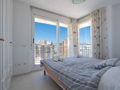 Habitación luminosa con cama doble, armario empotrado y acceso a terraza. Vistas urbanas despejadas bajo un cielo azul.