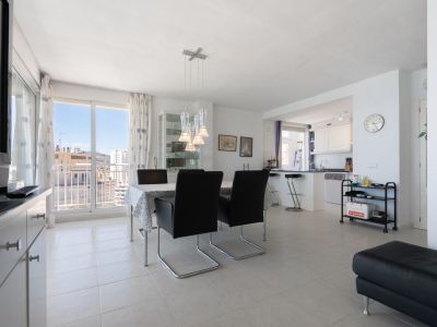 Luminoso salón-comedor de concepto abierto con lámpara colgante moderna, suelo de baldosas y acceso a balcón con vistas urbanas, junto a cocina semiabierta.
