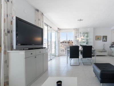 Salón-comedor luminoso con suelo de baldosas claras, TV en mueble gris y acceso a terraza con vistas urbanas, complementado por un área de comedor moderna.