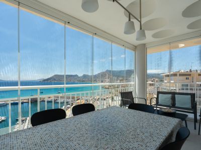 Terraza acristalada con zona de comedor, ofreciendo vistas directas al puerto deportivo de Calpe, el mar turquesa y el icónico Peñón de Ifach.