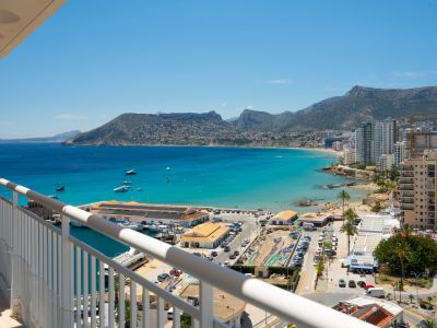 Vistas panorámicas desde la terraza al puerto de Calpe, la bahía de aguas turquesas y la costa con edificios y montañas al fondo.