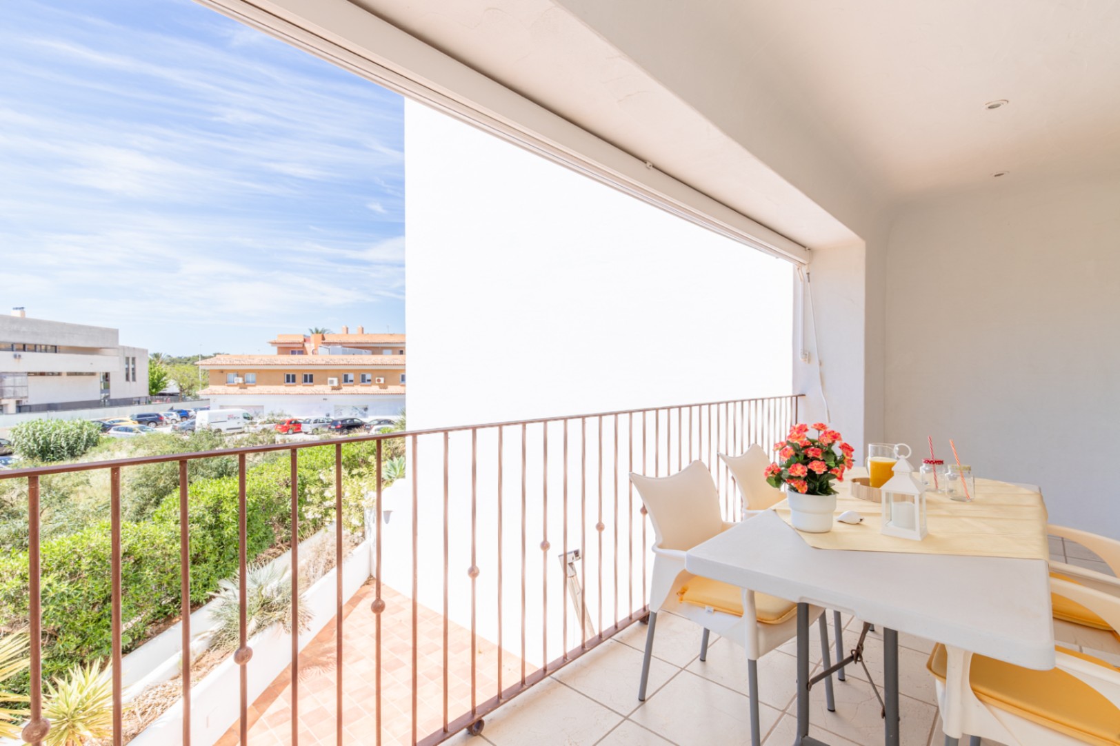Amplia terraza privada con suelo de baldosas y barandilla de metal, equipada con mesa y sillas para comedor exterior. Disfrute de vistas a la vegetación y edificios locales bajo un cielo despejado.