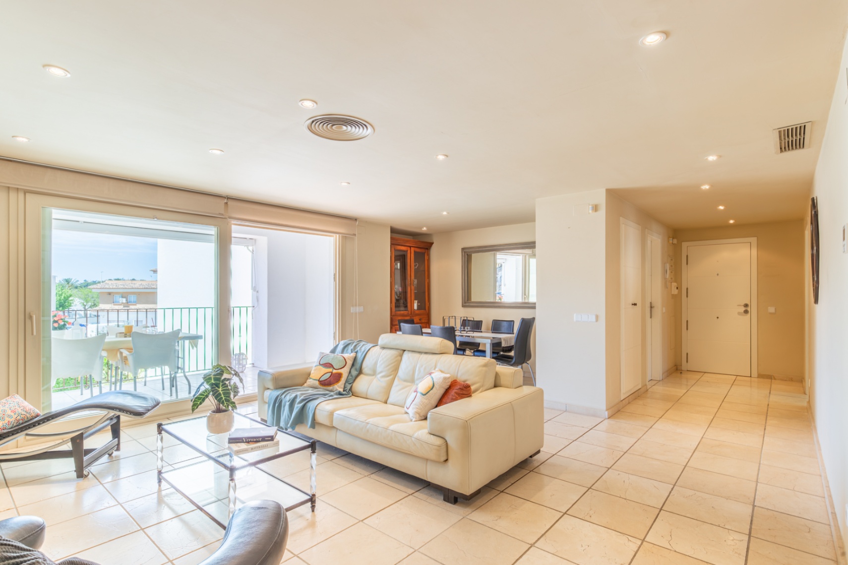Amplio salón-comedor de planta abierta con sofá de cuero crema y acceso directo a una terraza privada, inundado de luz natural y con suelo de gres claro.