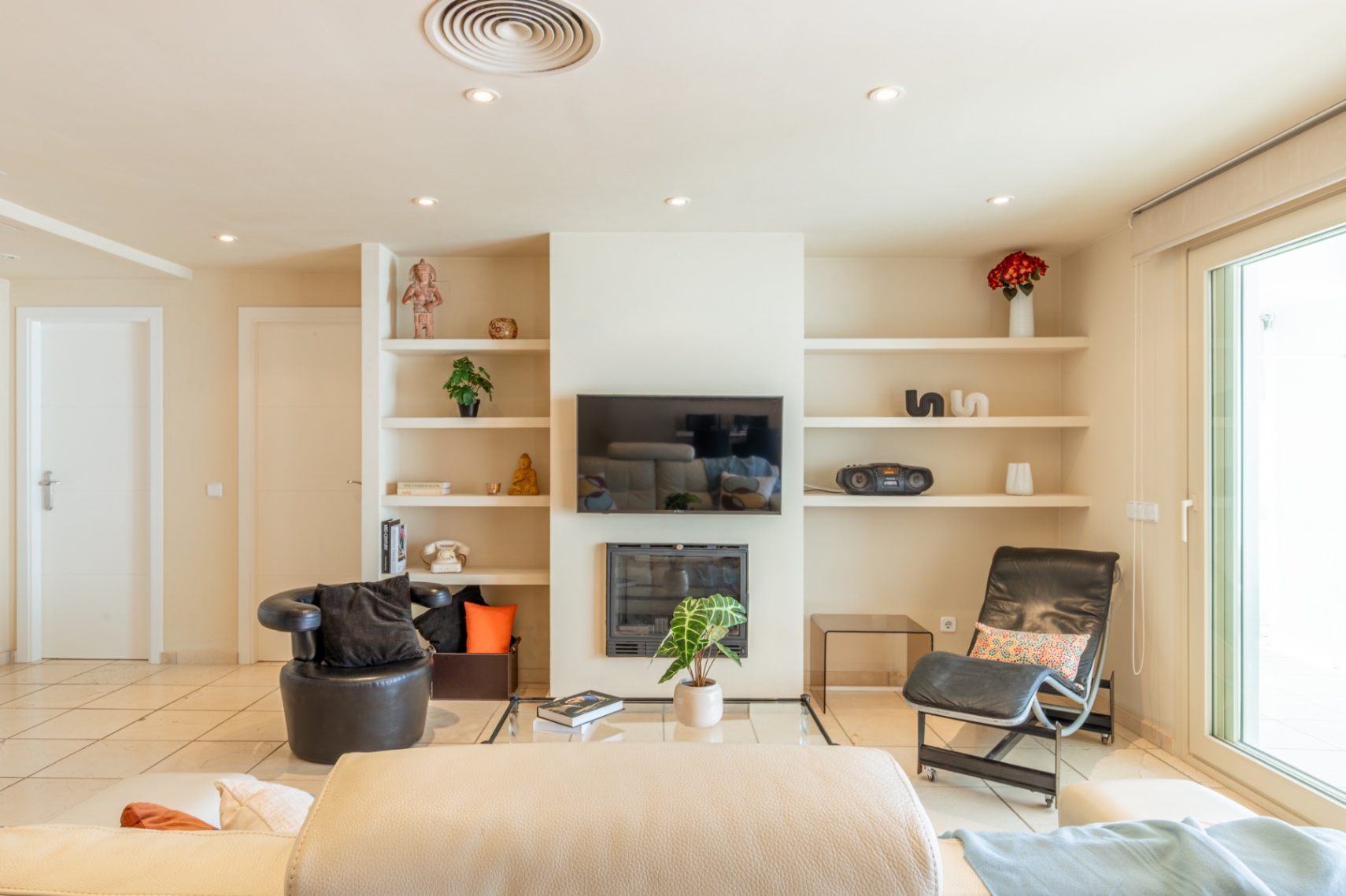 Amplio salón con suelo de baldosas claras, chimenea moderna y TV integrada. Destacan estanterías empotradas con decoración y una gran puerta corredera que aporta luz natural.