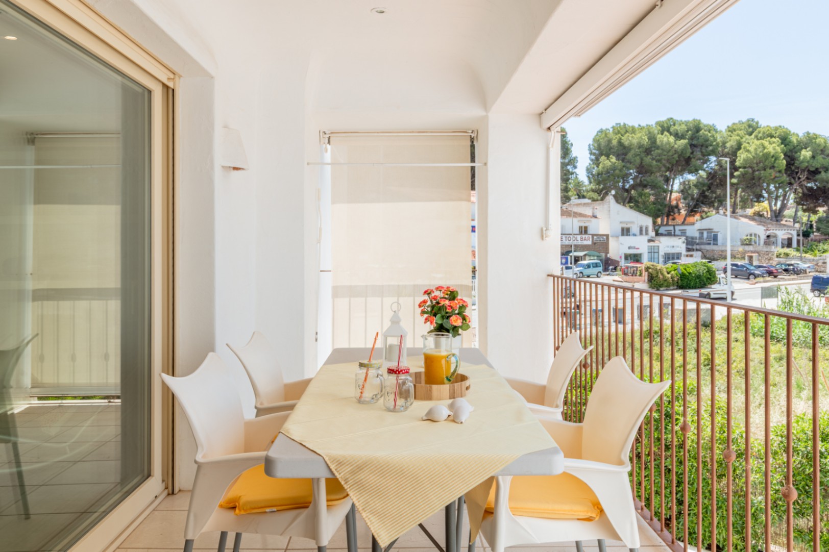 Luminosa terraza privada con mesa de comedor para cuatro personas y vistas a la calle y vegetación, accesible desde un amplio ventanal corredero.