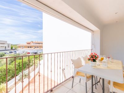 Amplia terraza privada con suelo de baldosas y barandilla de metal, equipada con mesa y sillas para comedor exterior. Disfrute de vistas a la vegetación y edificios locales bajo un cielo despejado.