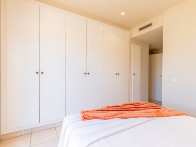Amplio armario empotrado de puertas paneladas blancas y tiradores oscuros, ofreciendo gran capacidad de almacenamiento en este luminoso dormitorio con suelo de baldosa.