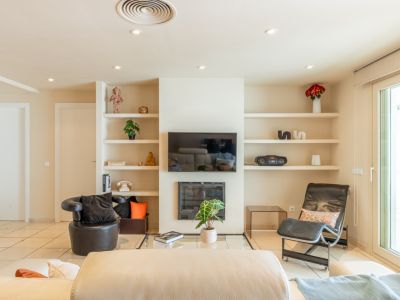 Amplio salón con suelo de baldosas claras, chimenea moderna y TV integrada. Destacan estanterías empotradas con decoración y una gran puerta corredera que aporta luz natural.