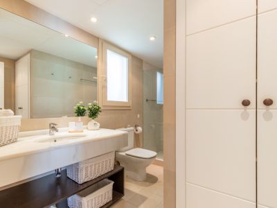 Baño completo con lavabo de mármol, amplio espejo y armarios empotrados. Incluye ducha con mampara de cristal, ventana discreta y detalles decorativos. Tonalidades neutras y gran capacidad de almacenamiento.