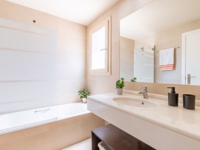 Baño moderno con lavabo flotante blanco, espejo grande y bañera con mampara de cristal a rayas, todo en un entorno de azulejos neutros.