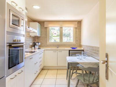 Cocina funcional con electrodomésticos de acero inoxidable integrados, encimera clara y salpicadero de ladrillo. Incluye una mesa compacta y ventana con vistas a la vegetación.
