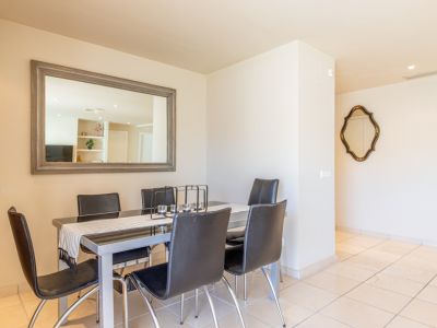 Comedor con mesa de cristal negro y seis sillas, complementado por un gran espejo con marco gris que amplía el espacio y un espejo decorativo. Suelo de baldosas claras.