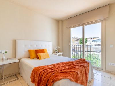 Dormitorio principal con cama doble, cabecero tapizado y suelo de baldosas claras. Acceso directo a un balcón con vistas urbanas.