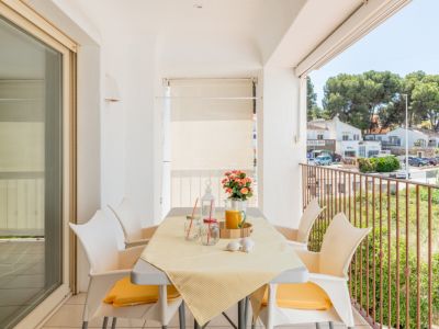 Luminosa terraza privada con mesa de comedor para cuatro personas y vistas a la calle y vegetación, accesible desde un amplio ventanal corredero.