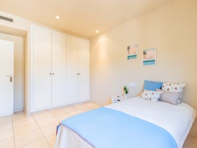 Luminoso dormitorio con amplios armarios empotrados blancos, suelo de baldosas claras y una cama confortable con decoración temática costera. Iluminación empotrada.