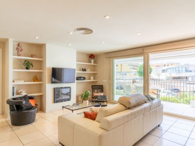 Luminoso salón con sofá crema, suelo de baldosas y estanterías empotradas junto a chimenea y TV. Grandes puertas correderas dan a una terraza privada con vistas urbanas.