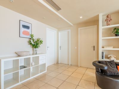 Recibidor funcional con suelo de gres claro, estanterías blancas modulares y empotradas, y tres puertas interiores. Destaca la decoración con arte abstracto y un teléfono vintage.