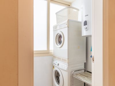 Zona de lavandería compacta con lavadora y secadora apiladas, optimizando el espacio. Dispone de calentador de agua y ventana con cristal opaco para luz natural.
