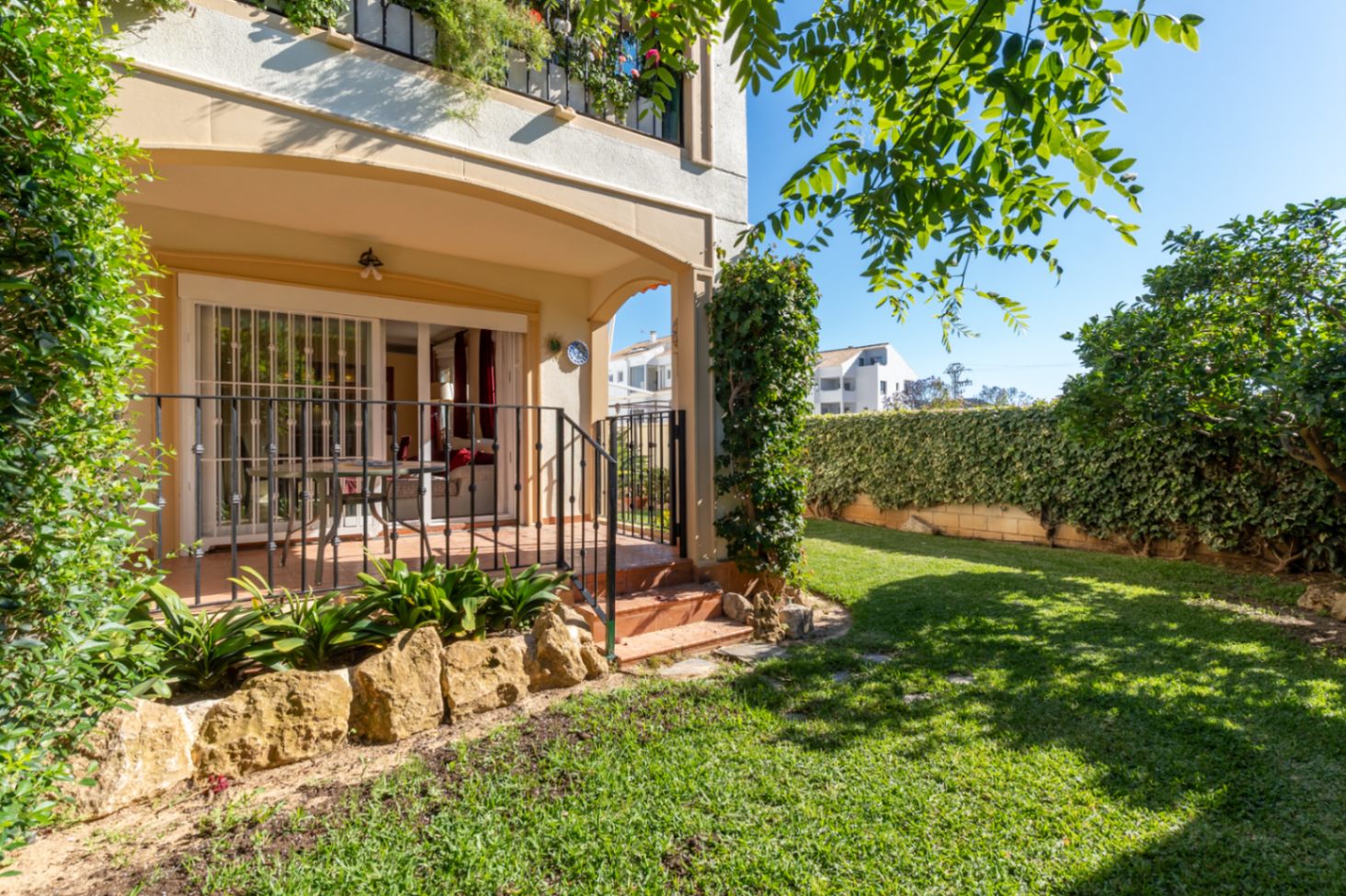 Amplio jardín privado con césped bien cuidado, rodeado de setos verdes. Incluye una terraza cubierta con acceso directo al interior, ideal para relajarse al aire libre.