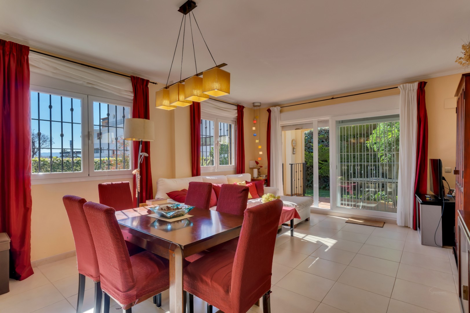 Amplio salón-comedor con mesa de madera para seis, sillas tapizadas en rojo y abundante luz natural. Acceso directo al jardín y ventanales con rejas de seguridad.