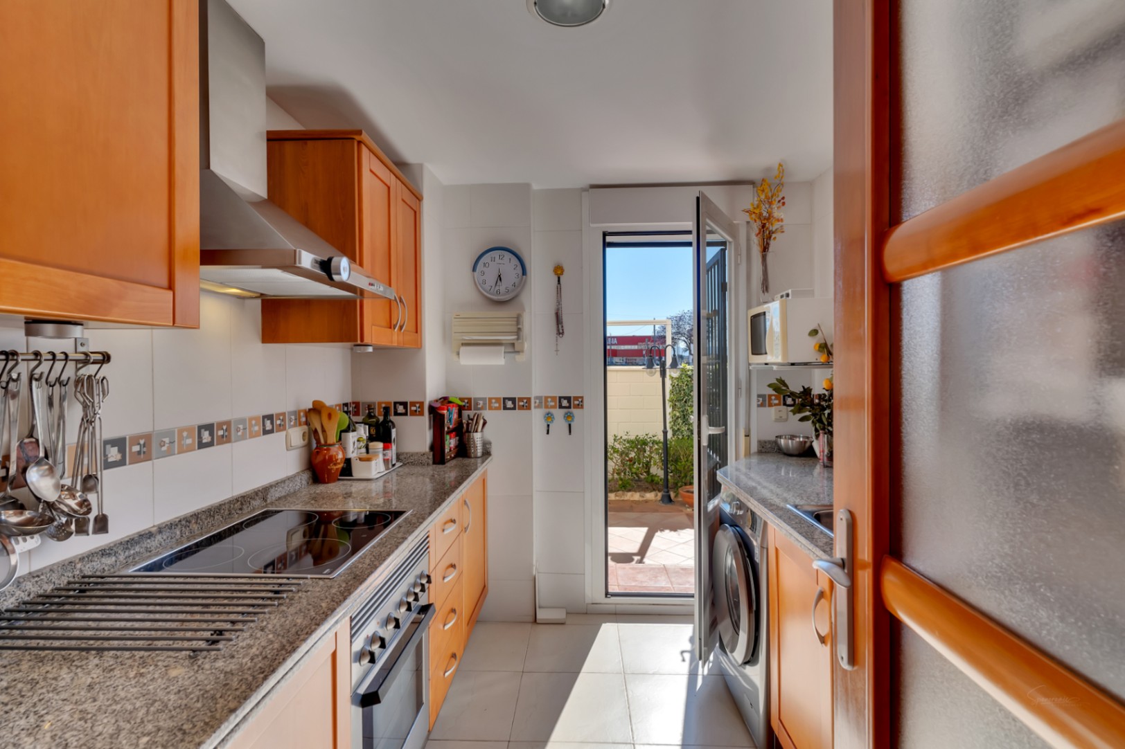 Cocina funcional con armarios de madera clara, encimeras de granito y electrodomésticos de acero inoxidable. Ofrece acceso directo a un patio exterior.