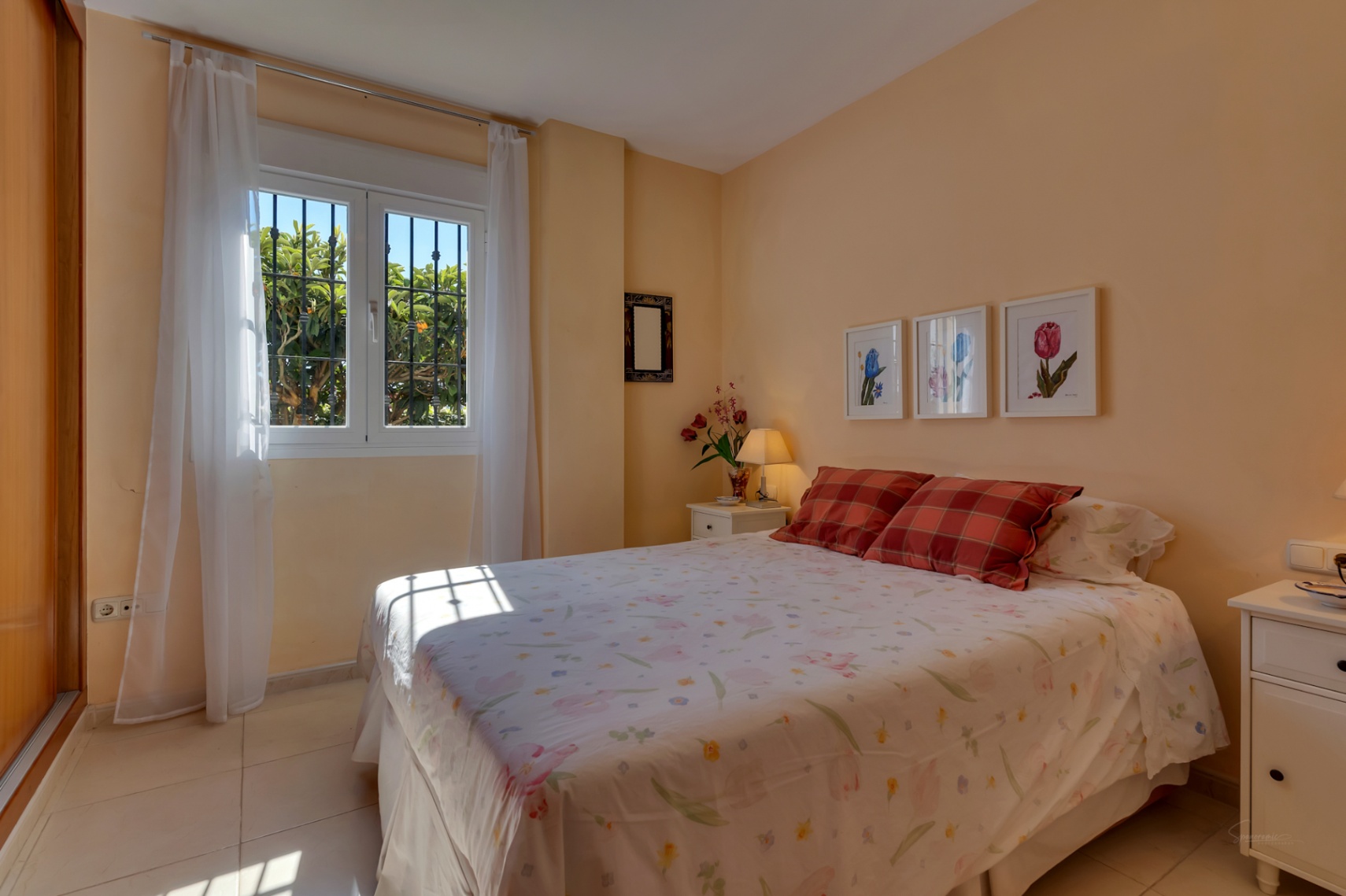 Luminoso dormitorio con paredes color melocotón, cama doble, y ventana con rejas que ofrece vistas al jardín y abundante luz natural. Incluye armario empotrado.