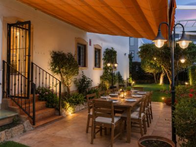 Acogedor comedor exterior en patio embaldosado, con gran mesa de madera preparada bajo toldo naranja retráctil y jardín privado iluminado.