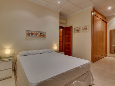 Acogedor dormitorio con cama doble, mesitas de noche modernas, amplio armario empotrado de madera y suelo de baldosas claras, complementado con aire acondicionado.